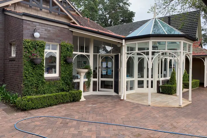 Dark brick house with a white glass conservatory and a brick-paved courtyard after cleaning, with a hose on the pavers.